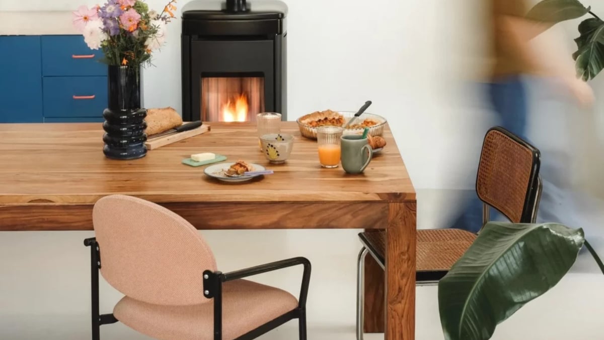 Poêle à granulés noir allumé dans une salle à manger avec table en bois, petit-déjeuner et chaises dépareillées
