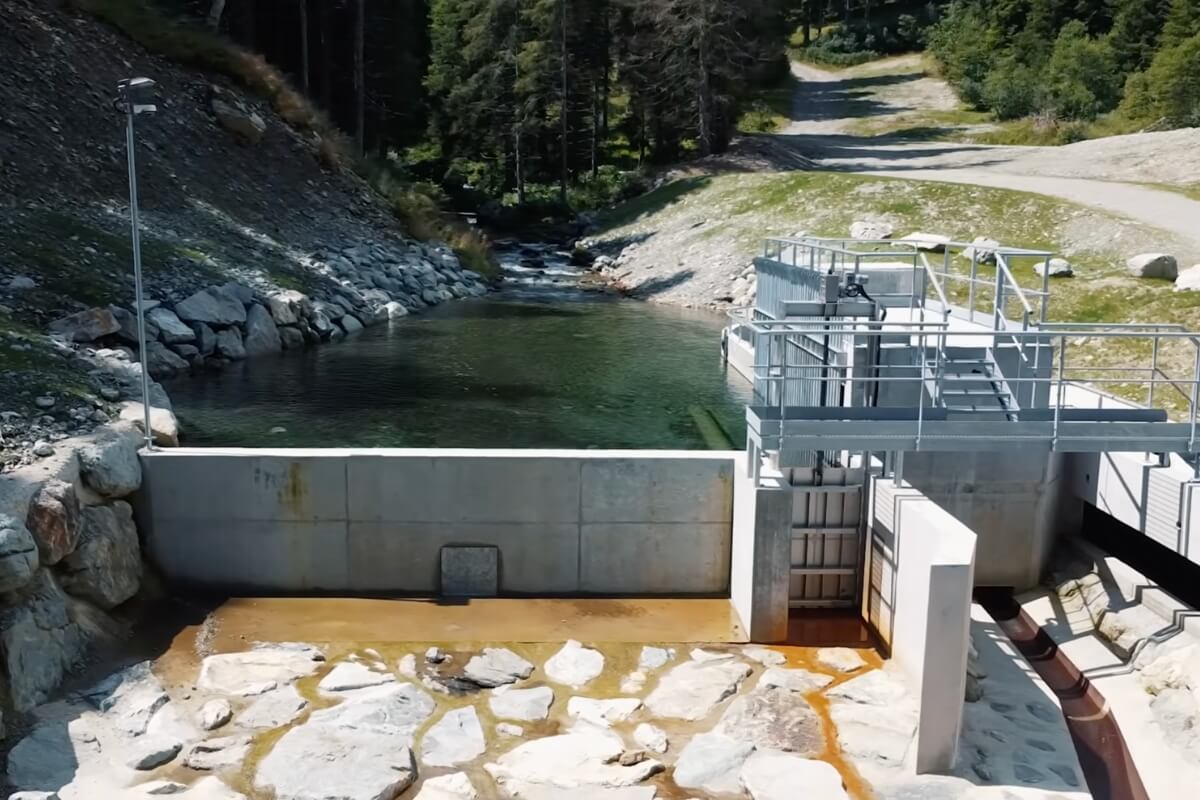 Le seuil en béton et la prise d'eau de la micro centrale hydroélectrique, montrant la vanne et le cours d'eau.