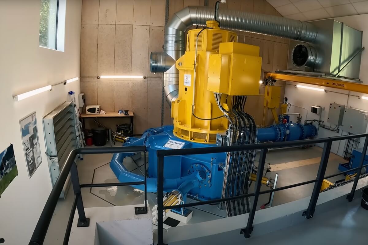 La turbine Pelton bleue et l'alternateur synchrone jaune au cœur de la salle des machines de la micro centrale hydroélectrique.